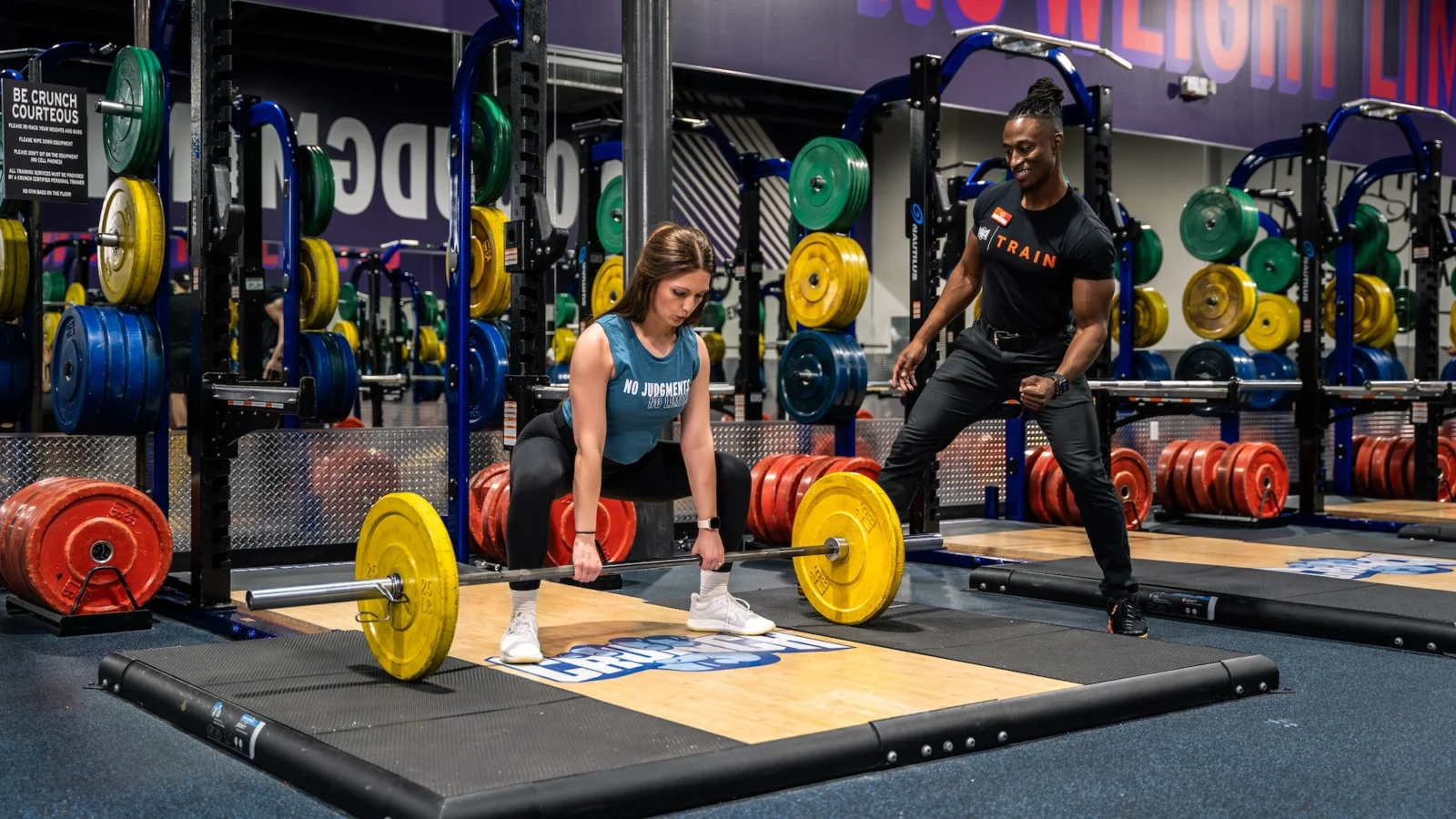 woman picks a barbell up off the ground next to her personal trainer