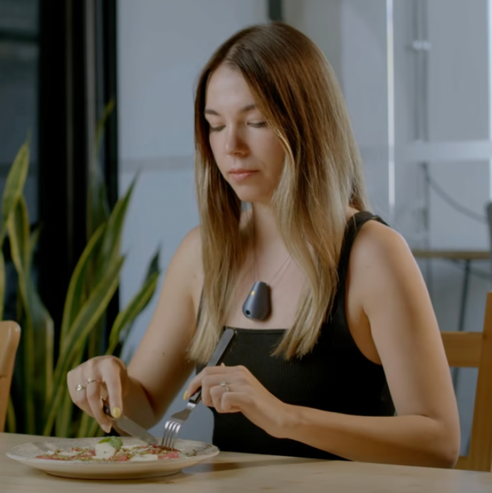 a woman eating a meal and wearing Rex.fit's The Drop, a wearable nutrition tracker.