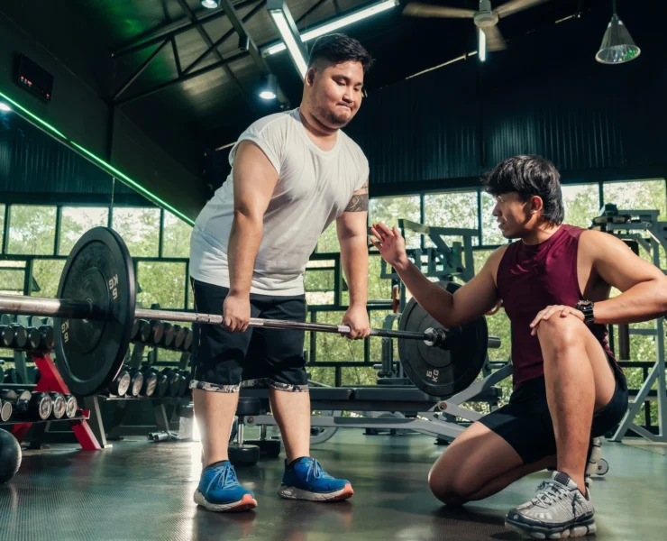 overweight man works out with help from a personal trainer