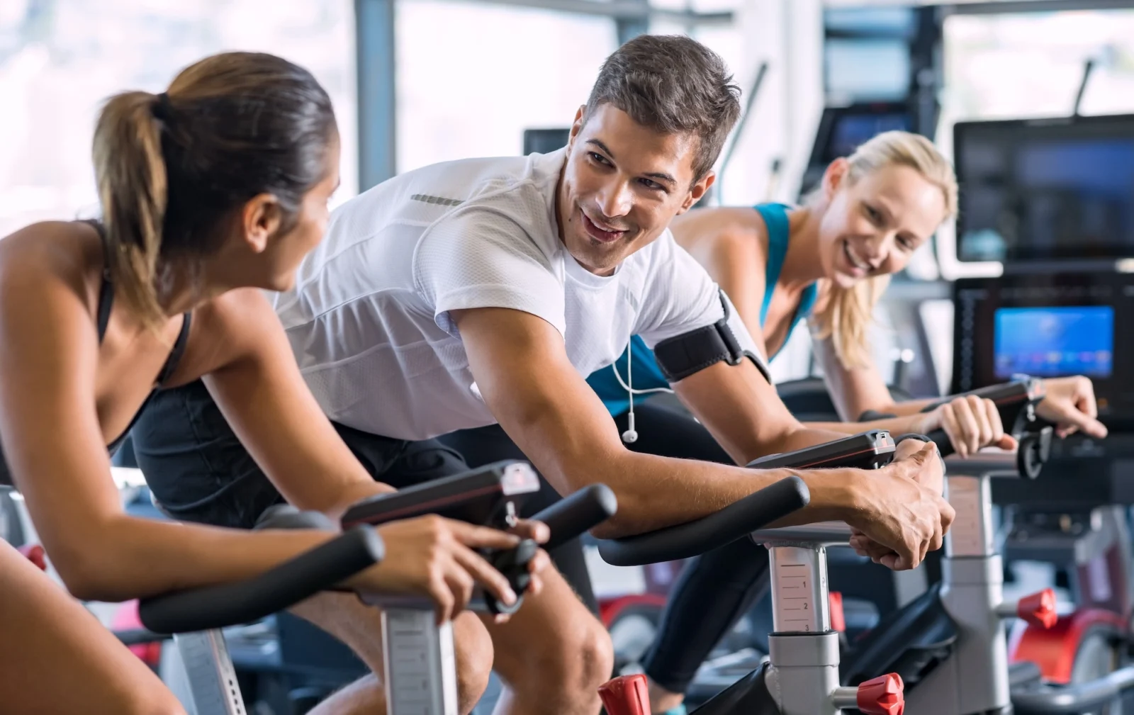 man and two women on indoor cycling bikes