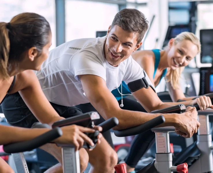 man and two women on indoor cycling bikes